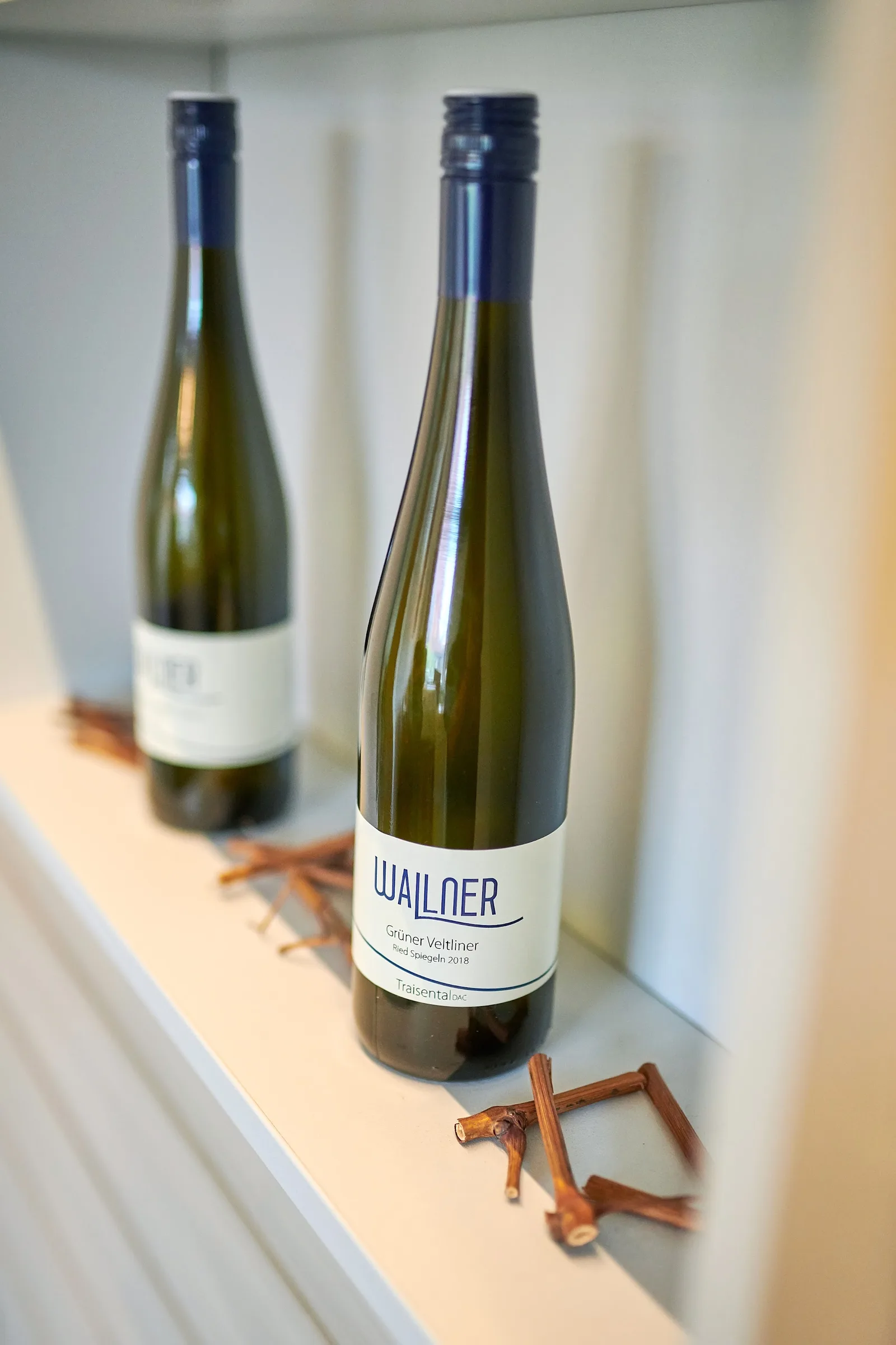 Zwei Flaschen Grüner Veltliner Ried Spiegeln Traisental DAC im Regal, daneben Rebholz